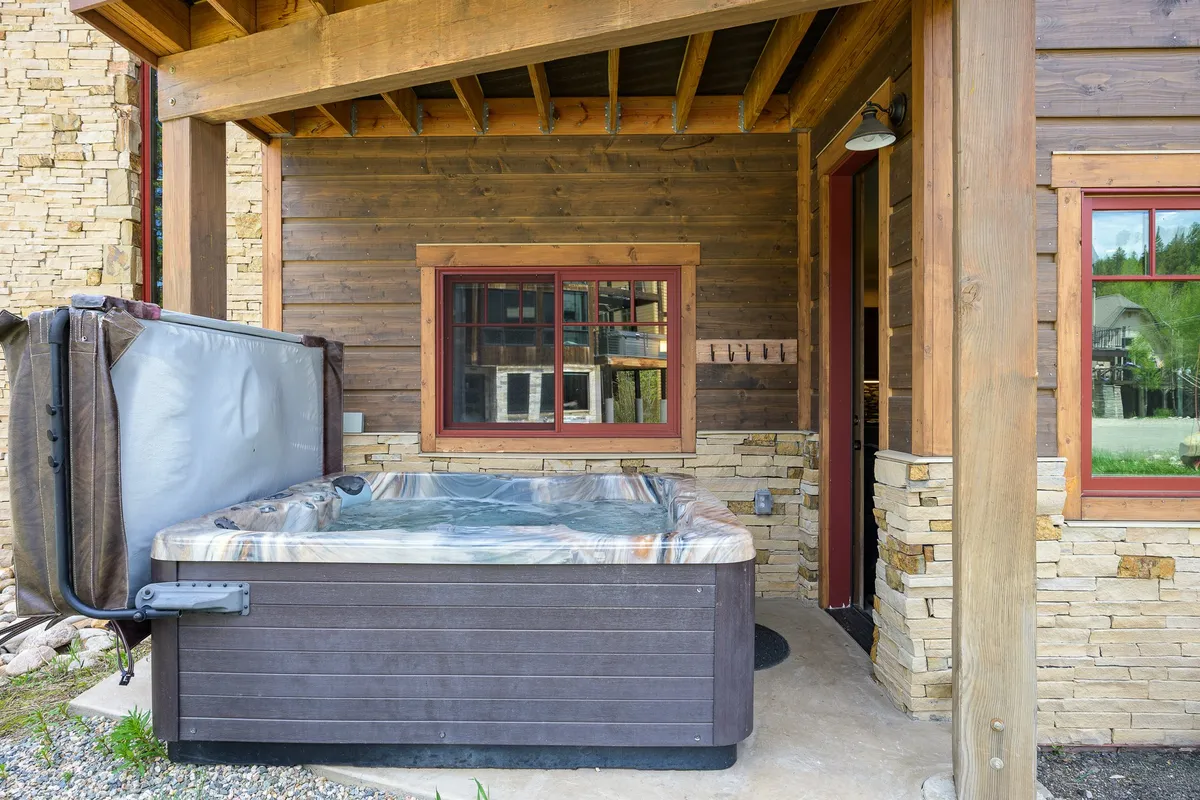 A tranquil hot tub sits beneath a wooden structure, surrounded by a stone wall and lush greenery. The setting exudes privacy and connection to nature, evoking relaxation and the opportunity to unwind while taking in the surrounding views—ideal for both stargazing at night and morning refreshment.