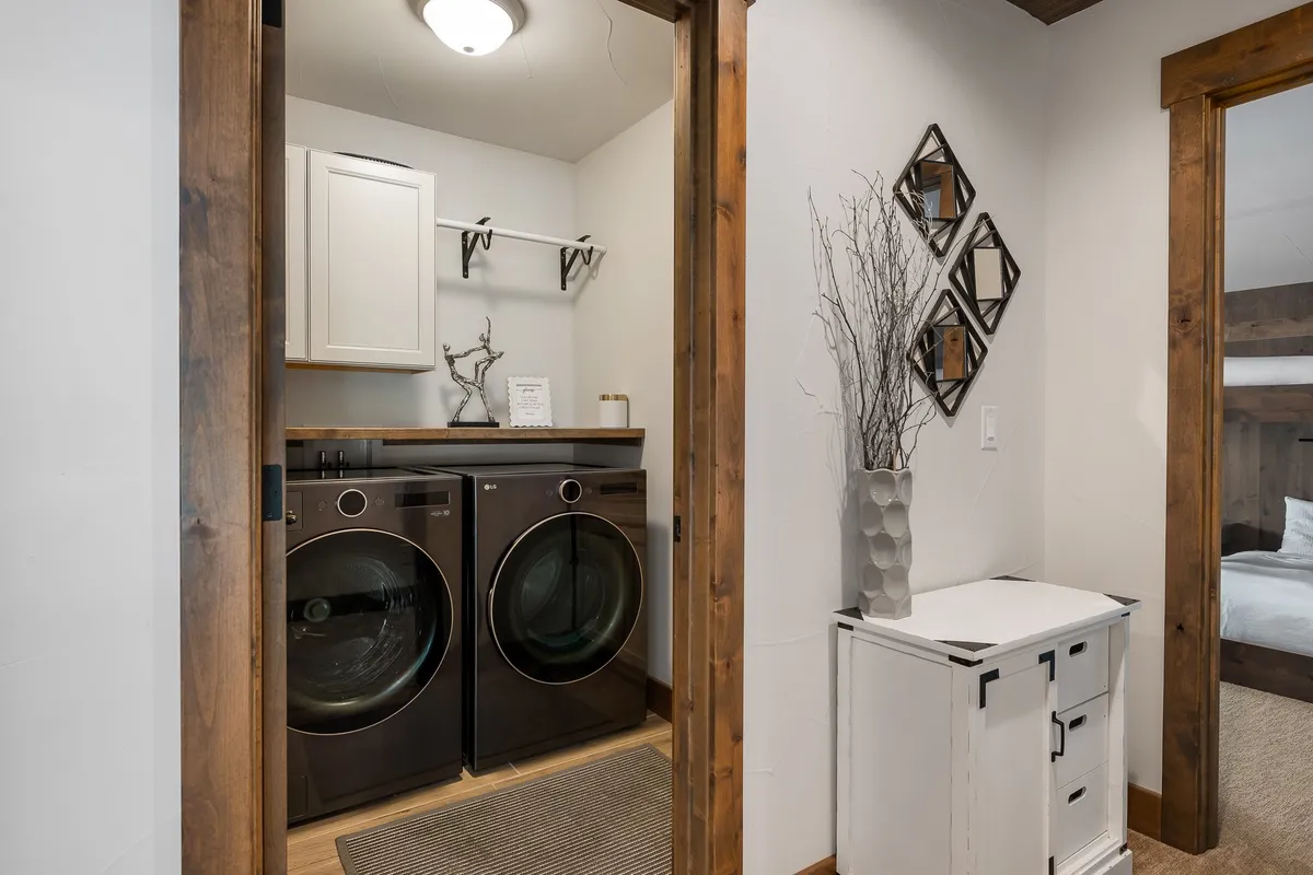 A bright and organized laundry area featuring a washer and dryer, a clean wood shelf above for storage, and decorative accents like a vase and mirrors that contribute to a sense of cleanliness and order.
