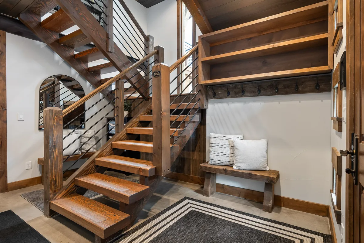 A welcoming entryway featuring a staircase, a simple bench, and tidy shelves, all presented in a fashion that feels both inviting and immaculately maintained.