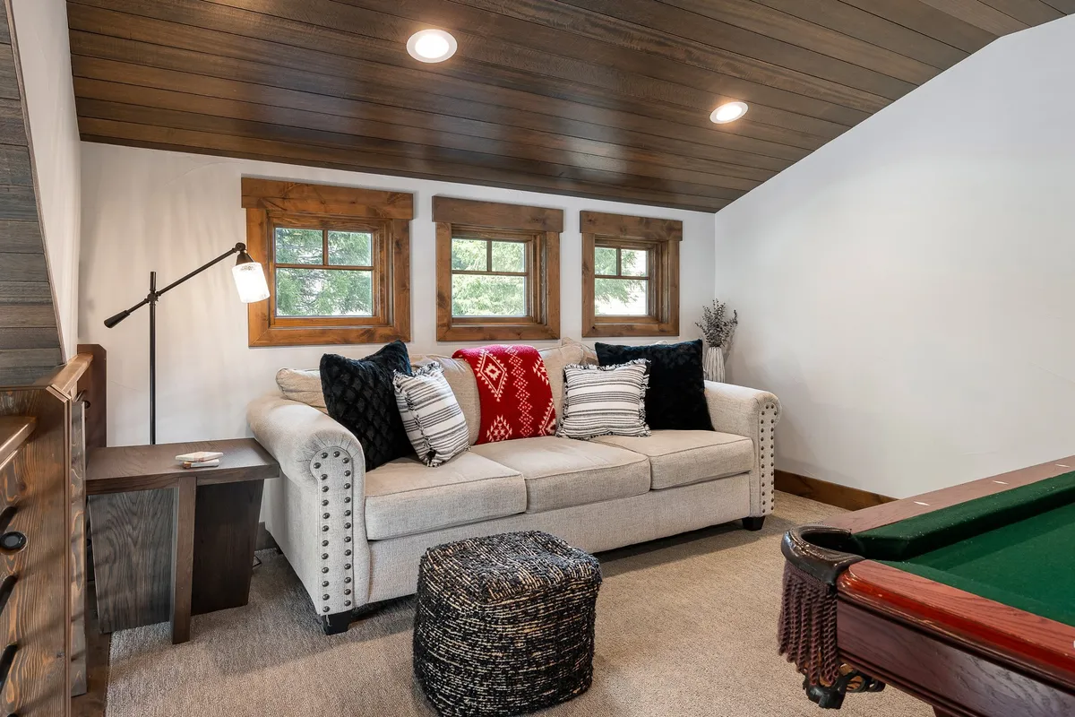 A spacious, well-lit area with both a pool table and a cozy sofa, set against a backdrop of large windows allowing plenty of natural light. The open layout supports group activities, relaxation, and memorable game nights.