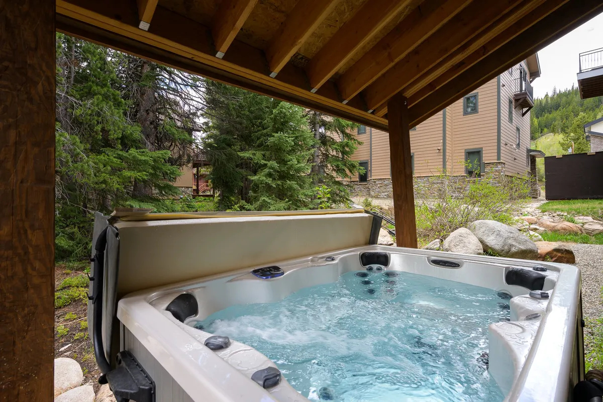 A tranquil exterior shot showcasing a hot tub nestled among lush greenery with the building facade visible behind. The scene suggests relaxation, socializing, and the enjoyment of natural surroundings, especially suitable for chilly evenings or post-adventure unwinding.