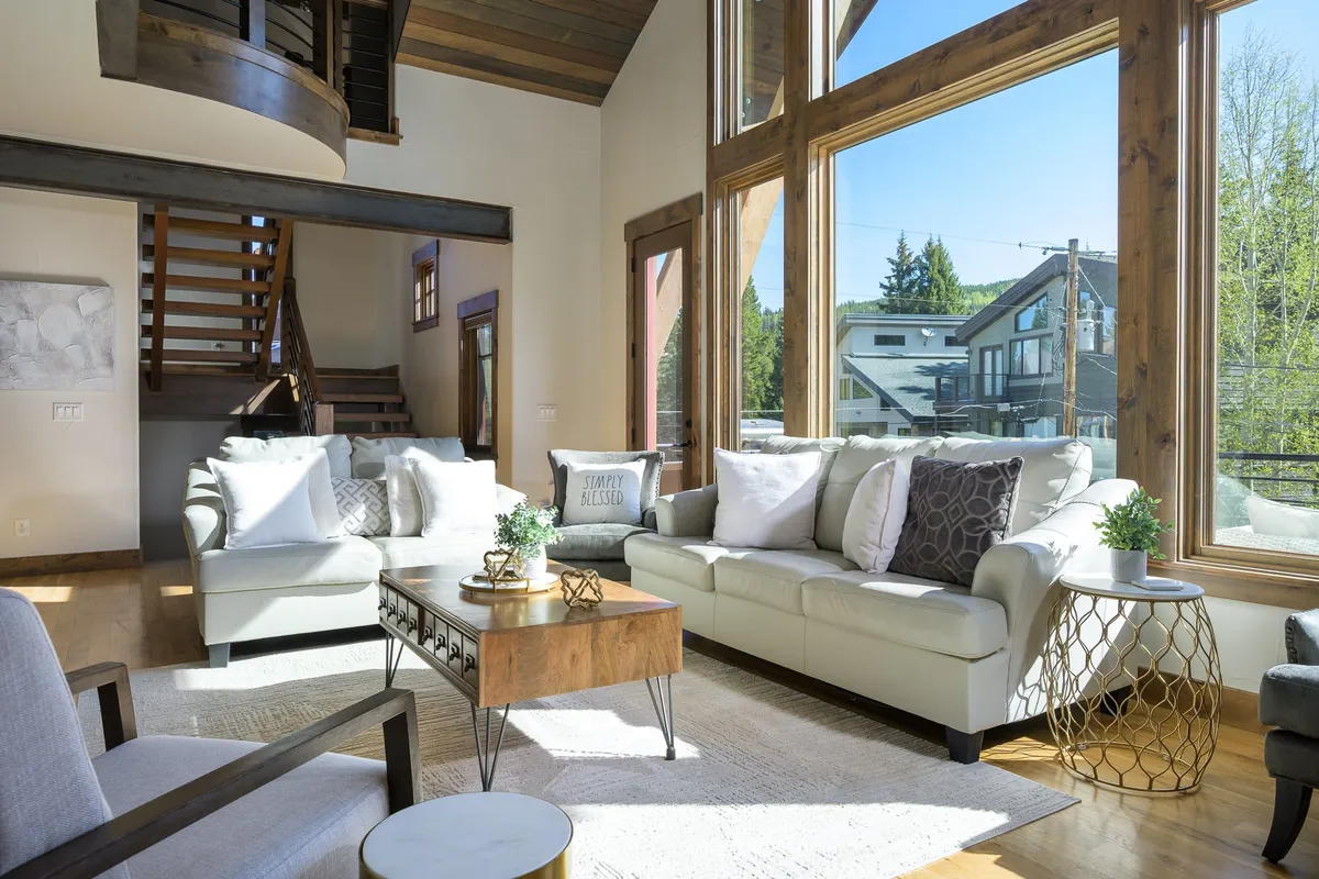 A modern living space filled with natural light from large windows, furnished with comfortable, clean-lined modern furniture and a decorative coffee table. The room exudes an uncluttered, inviting atmosphere that feels fresh and welcoming.