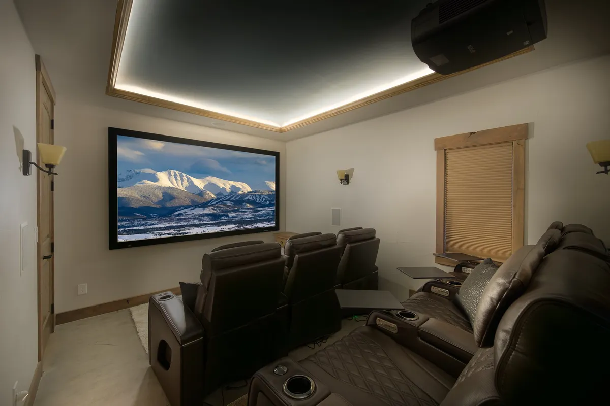 A state-of-the-art theatre room with luxurious leather seating, a large screen displaying a mountain landscape, and soft ambient lighting. The setup promises an immersive, comfortable experience ideal for movie marathons or big game nights with friends and family.