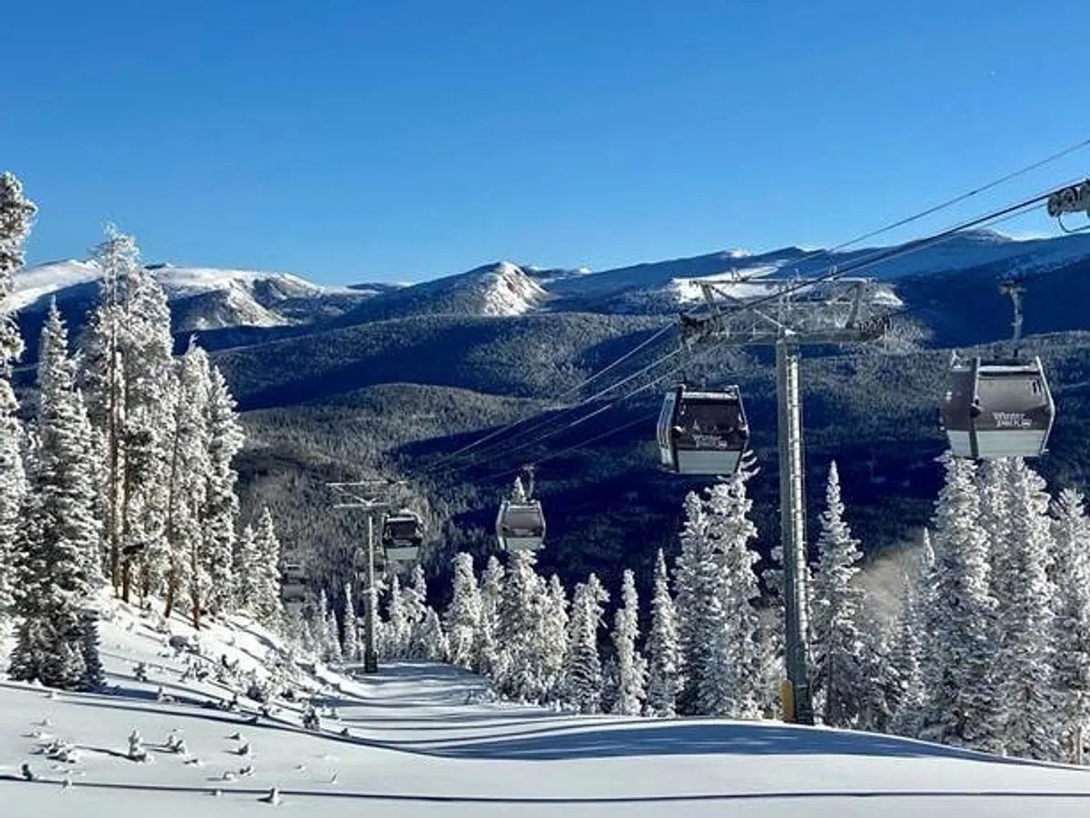 A serene winter landscape featuring a ski lift ascending over a snow-covered terrain, with distant mountain peaks providing a stunning backdrop. The image captures the essence of a day spent on the slopes and the natural beauty of Winter Park.